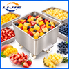 Stainless steel food preparation bin surrounded by washed and cut vegetables including broccoli, carrots and peppers